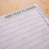 49x70cm 2024 wall planner. Runs from January to December 2024 and includes week numbers and moon phases. Designed with colourful abstract shapes. 100% Recycled Paper. Made in the UK.