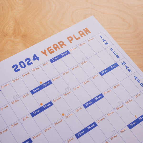 A1 size wall planner. 2024 year planner, January to December. Blue and Burnt Orange with a sunrise and quote. Highlighed weekends, week numbers and moon phases. 100% Recycled Paper. Made in the UK.