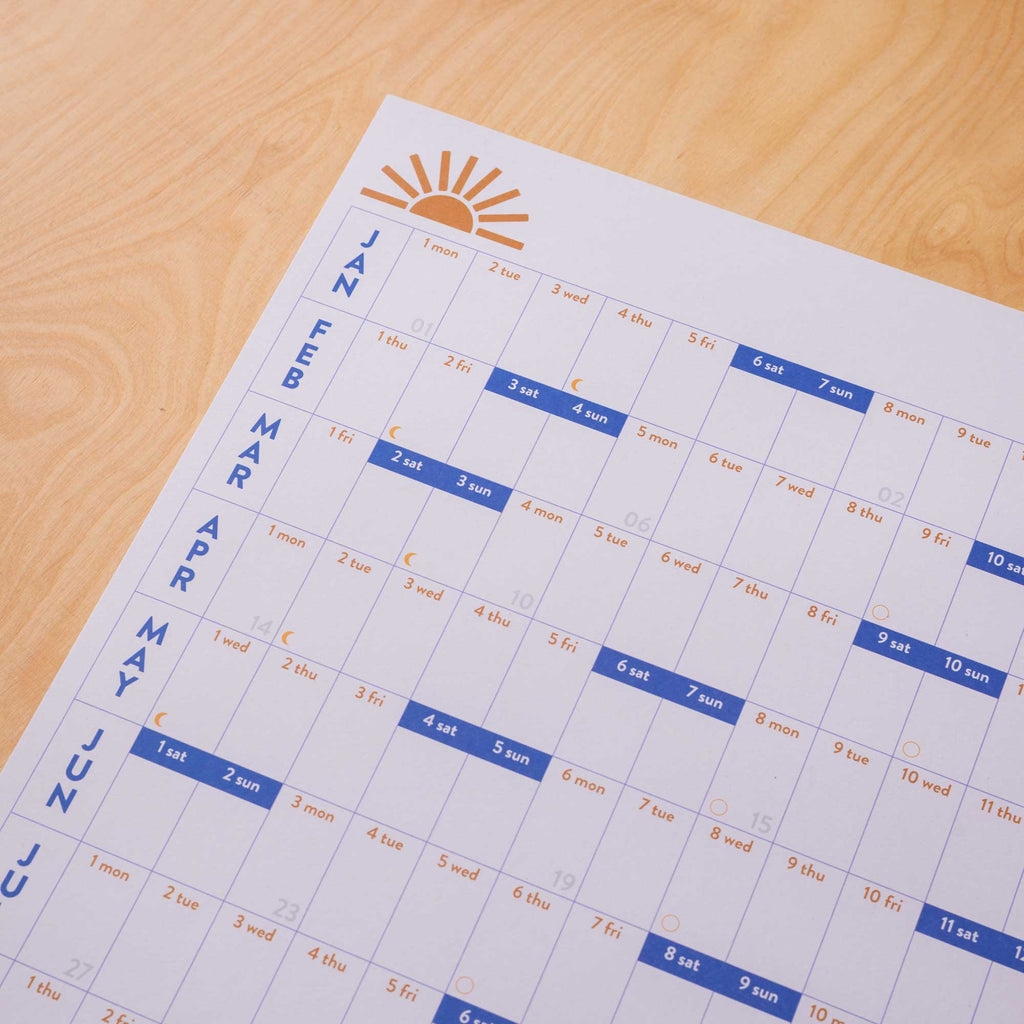A1 size wall planner. 2024 year planner, January to December. Blue and Burnt Orange with a sunrise and quote. Highlighed weekends, week numbers and moon phases. 100% Recycled Paper. Made in the UK.